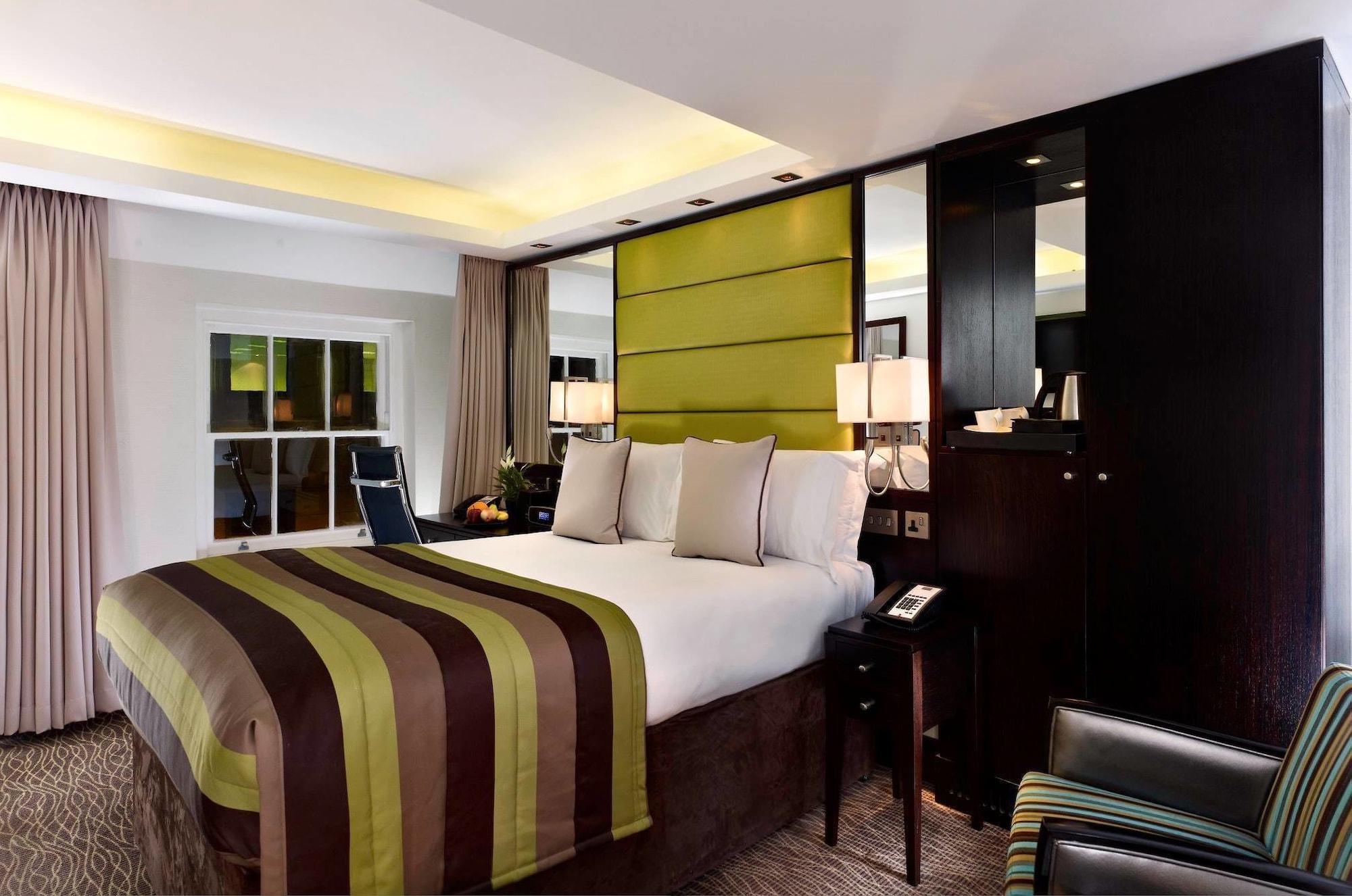 Montcalm Brewery Townhouse Hotel London Ngoại thất bức ảnh The photo shows a modern hotel room featuring a large bed with a striped comforter in shades of green, brown, and cream. The bed is adorned with several decorative pillows. Behind the bed, there is a contemporary headboard with a green panel design. 