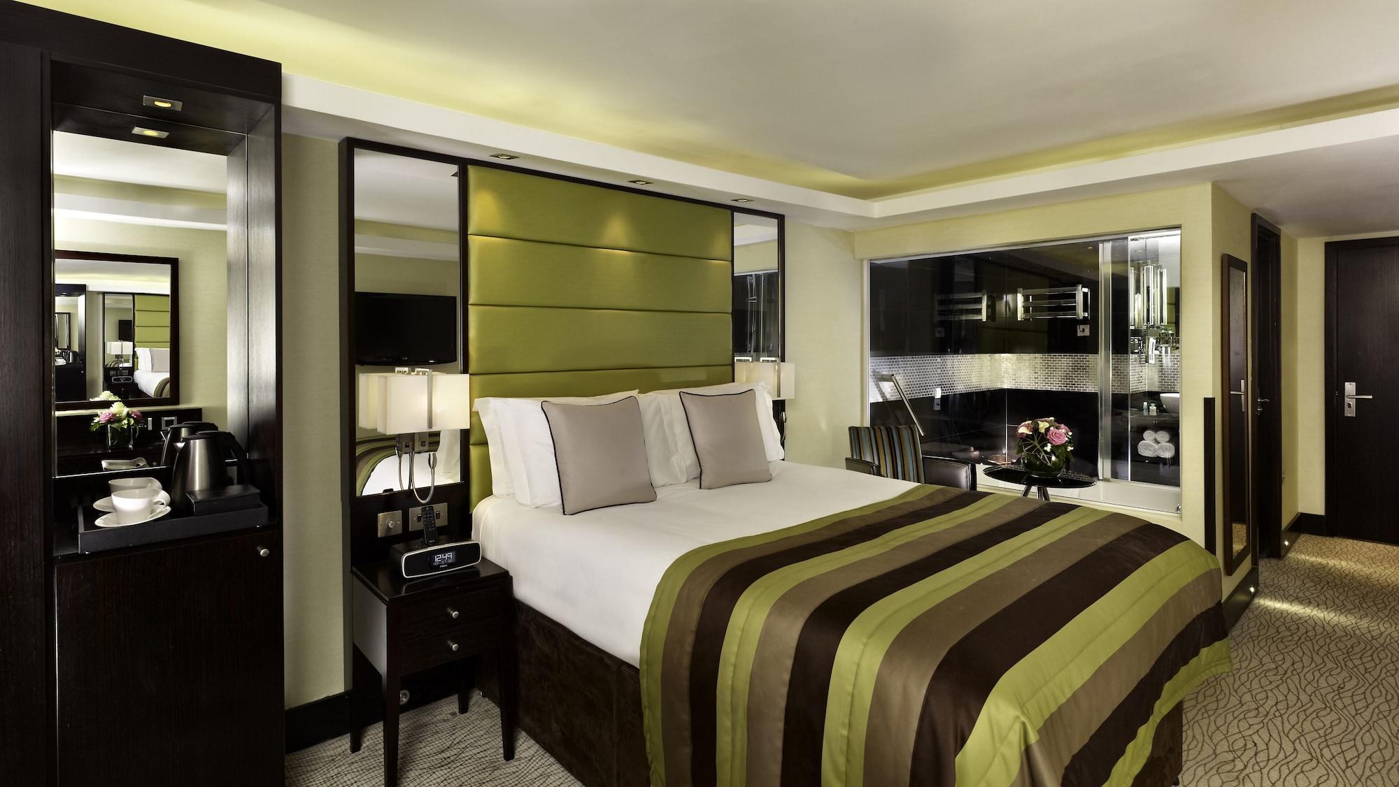 Montcalm Brewery Townhouse Hotel London Ngoại thất bức ảnh The photo shows a modern hotel room designed with a sophisticated aesthetic. It features a comfortable double bed with a striped brown and green bedspread, complemented by two light gray decorative pillows. Behind the bed is an elegant headboard sect