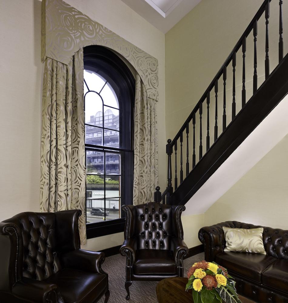 Montcalm Brewery Townhouse Hotel London Ngoại thất bức ảnh The photo shows a cozy interior space featuring two elegant leather armchairs placed near a large, ornate window with arched top and decorative curtains. The wall is painted in a muted color, enhancing the warmth of the room. A staircase with black s
