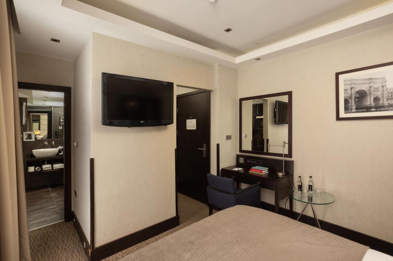 Montcalm Brewery Townhouse Hotel London Ngoại thất bức ảnh The photo shows a hotel room featuring a double bed with a neutral-colored bedspread. On one wall, there is a flat-screen TV mounted. Adjacent to the bed, there is a stylish desk with a chair and a small glass table. A mirror is positioned above the 