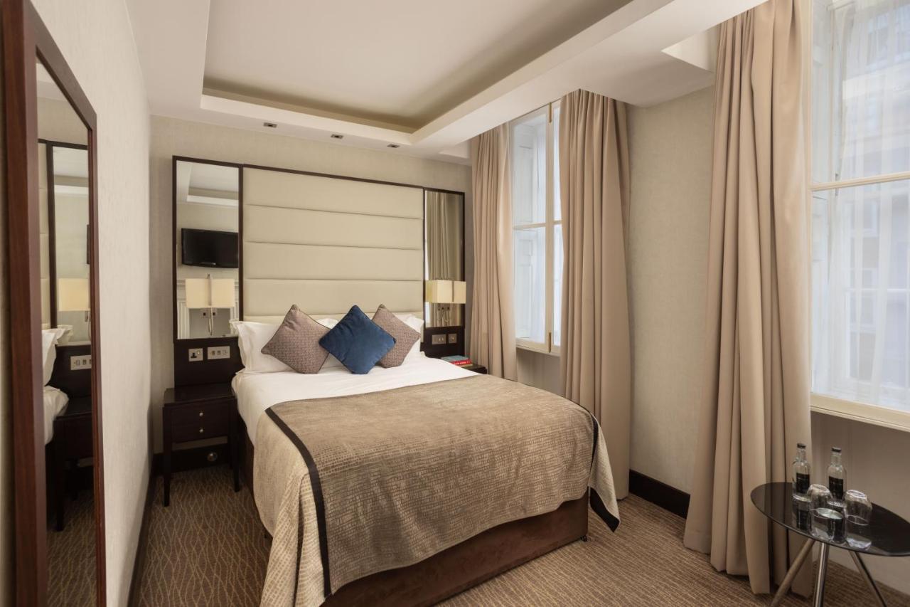 Montcalm Brewery Townhouse Hotel London Ngoại thất bức ảnh The photo shows a cozy hotel bedroom. The room features a neatly made double bed with a beige bedspread and decorative pillows, including a blue one. There are bedside tables on either side of the bed with lamps. The walls are painted in a soft color