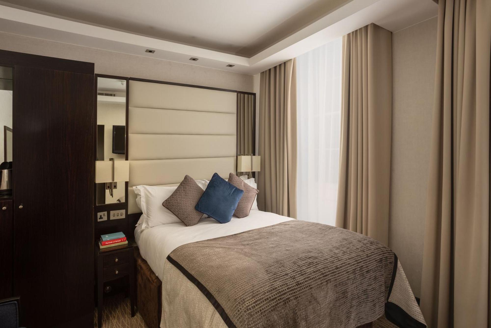 Montcalm Brewery Townhouse Hotel London Ngoại thất bức ảnh The photo shows a modern hotel room with a cozy design. It features a double bed with a light-colored headboard and a soft, stylish blanket. There are decorative pillows on the bed, including a blue one. On either side of the bed, there are small nig