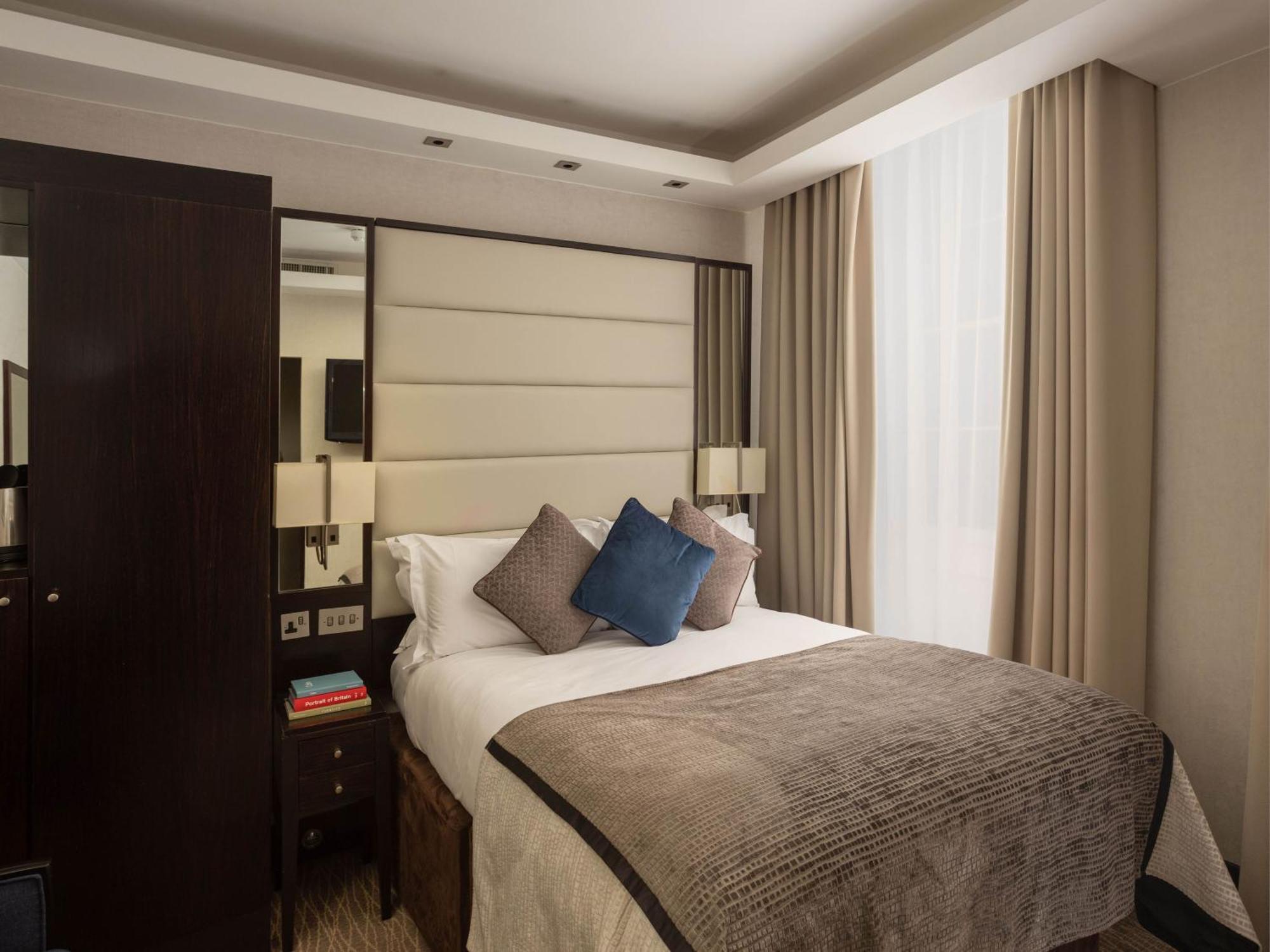 Montcalm Brewery Townhouse Hotel London Ngoại thất bức ảnh The image shows a cozy bedroom. It features a comfortable double bed with a light-colored duvet and decorative pillows in shades of blue and gray. The headboard is upholstered in a soft material, and there are bedside lamps on either side of the bed.