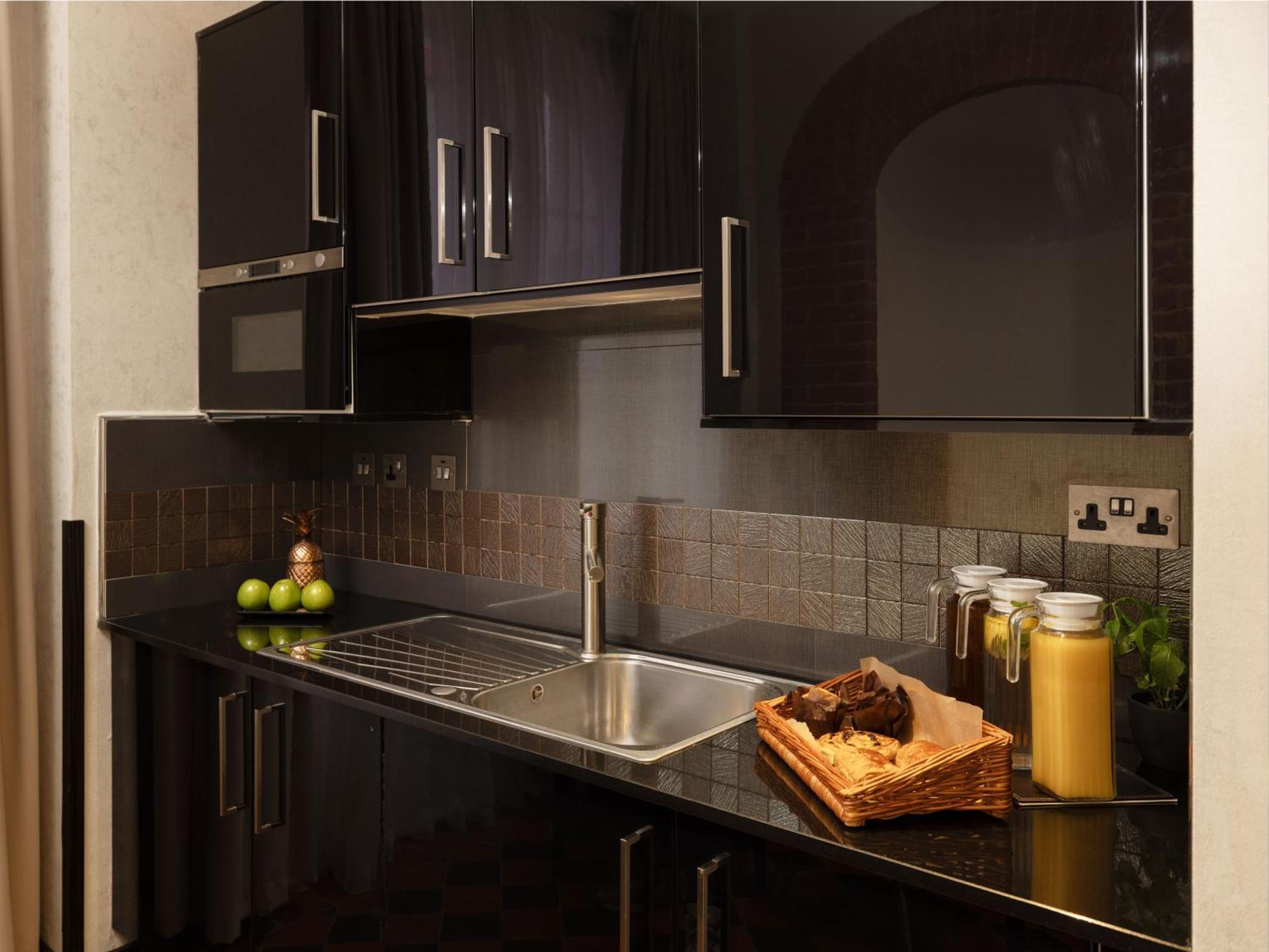 Montcalm Brewery Townhouse Hotel London Ngoại thất bức ảnh The photo shows a modern kitchen with sleek black cabinetry and a glossy finish. The kitchen features a stainless steel sink with a contemporary faucet, set against a dark, textured countertop. Above the counter, there are cabinets that match the cou