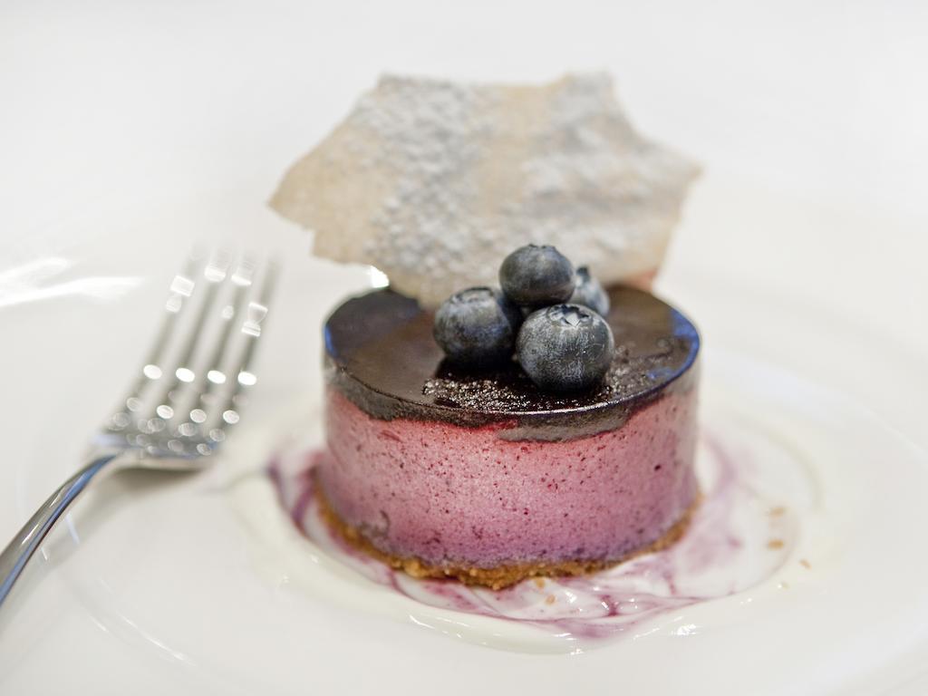 Montcalm Brewery Townhouse Hotel London Ngoại thất bức ảnh The photo shows a beautifully plated dessert, which appears to be a round cheesecake or mousse. It has a pinkish-purple filling, topped with a glossy dark chocolate layer. Three fresh blueberries sit on top, adding a pop of color. The dessert is acco
