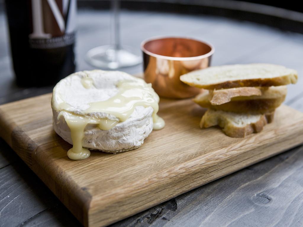 Montcalm Brewery Townhouse Hotel London Ngoại thất bức ảnh The photo features a wooden serving board with several items. There is a round cheese, likely Brie or a similar soft cheese, that appears to be melting and dripping slightly. Next to the cheese, there is a small copper cup that might contain a sauce 