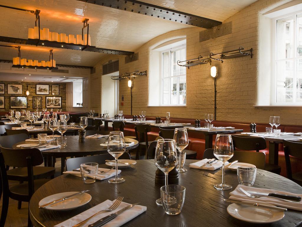 Montcalm Brewery Townhouse Hotel London Ngoại thất bức ảnh The photo shows a restaurant interior featuring a warm and inviting atmosphere. It has several round wooden tables set for dining, each with neatly arranged plates, utensils, and glasses. The lighting is soft, with overhead fixtures providing a cozy 
