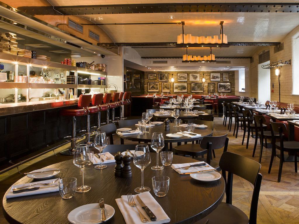 Montcalm Brewery Townhouse Hotel London Ngoại thất bức ảnh The photo shows the interior of a stylish restaurant. It features several round tables set with white plates, glasses, and silverware, all neatly arranged for dining. The decor includes a modern design with wooden floors and a mix of lighting fixture