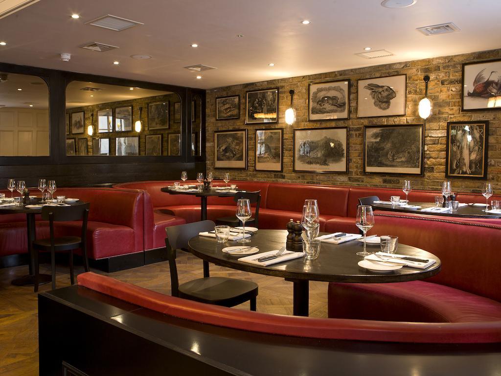Montcalm Brewery Townhouse Hotel London Ngoại thất bức ảnh The photo depicts an elegant restaurant interior. There are curved red booths along the walls, creating a cozy seating arrangement. The tables are round and set with white plates and glassware, indicating a prepared dining area. The walls feature a n