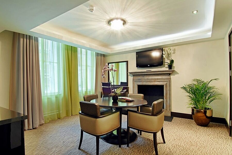 Montcalm Brewery Townhouse Hotel London Ngoại thất bức ảnh The photo shows a well-furnished room, likely a hotel suite or a modern living space. It features a round dining table with four comfortable chairs. The walls are adorned with light-colored decor, and there are large windows with sheer and solid curt