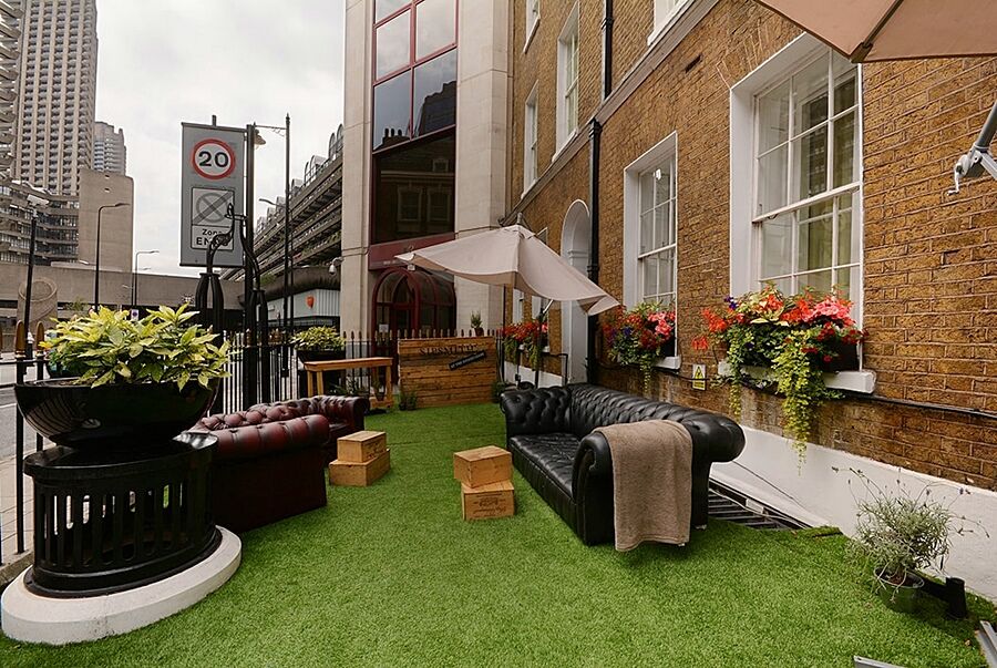 Montcalm Brewery Townhouse Hotel London Ngoại thất bức ảnh The photo depicts a charming outdoor space, likely a patio or garden area. It features two comfortable-looking leather sofas, one of which is a deep burgundy color, placed on a green artificial lawn. There are wooden crates that could serve as side t